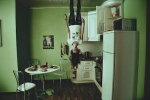 A person hangs upside down in a modern kitchen setting, creating a surreal ambiance.