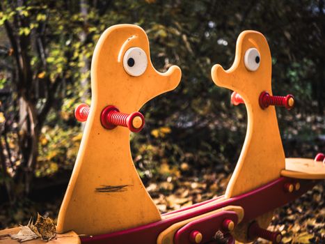 Colorful duck-themed seesaw in a playground amidst autumn foliage.