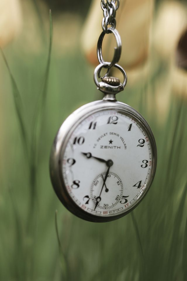 Close-up of a vintage pocket watch suspended outdoors with a blurred green background.